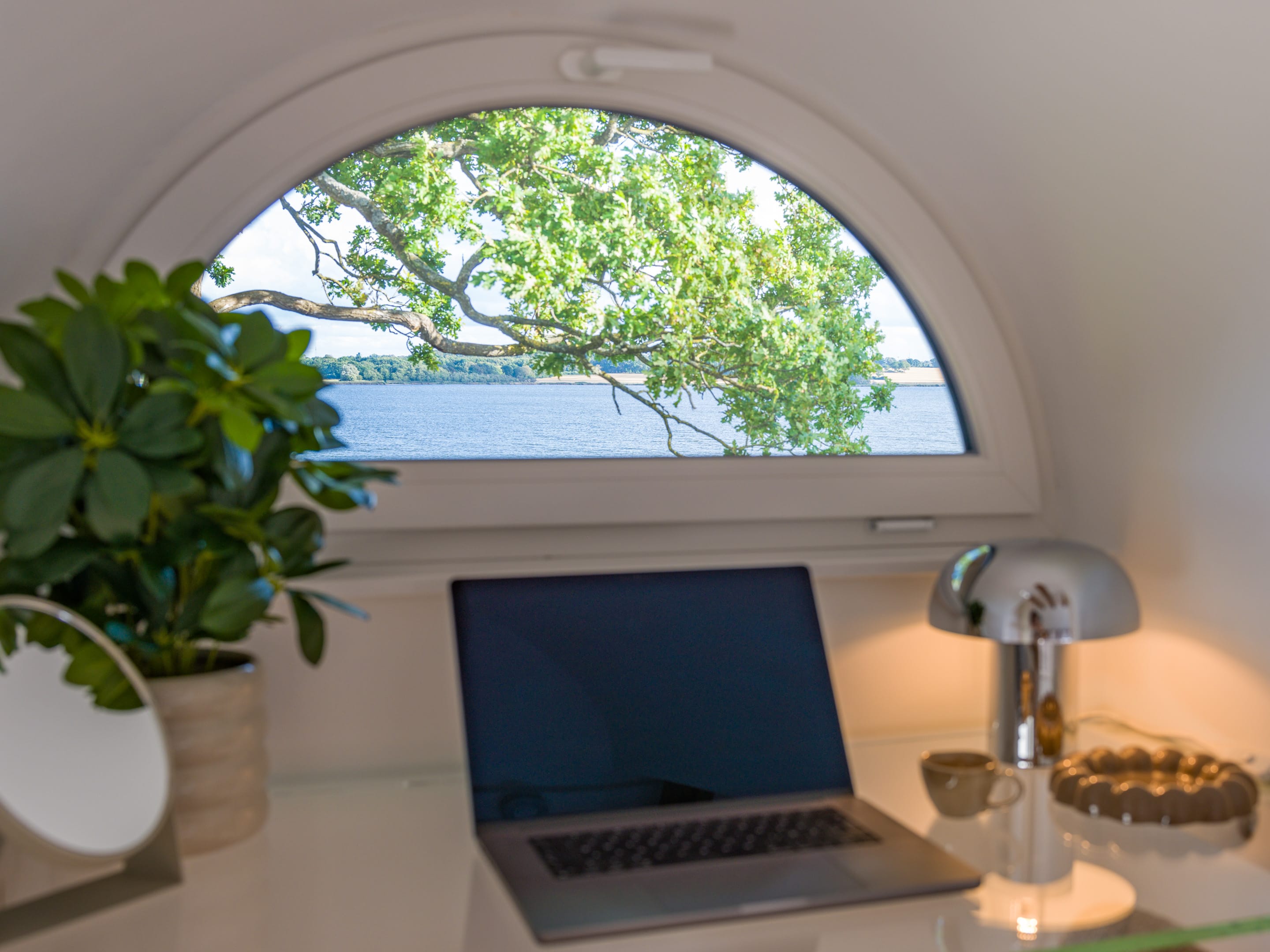 Glass desk beneath the arched dormer window with a view of the Schlei